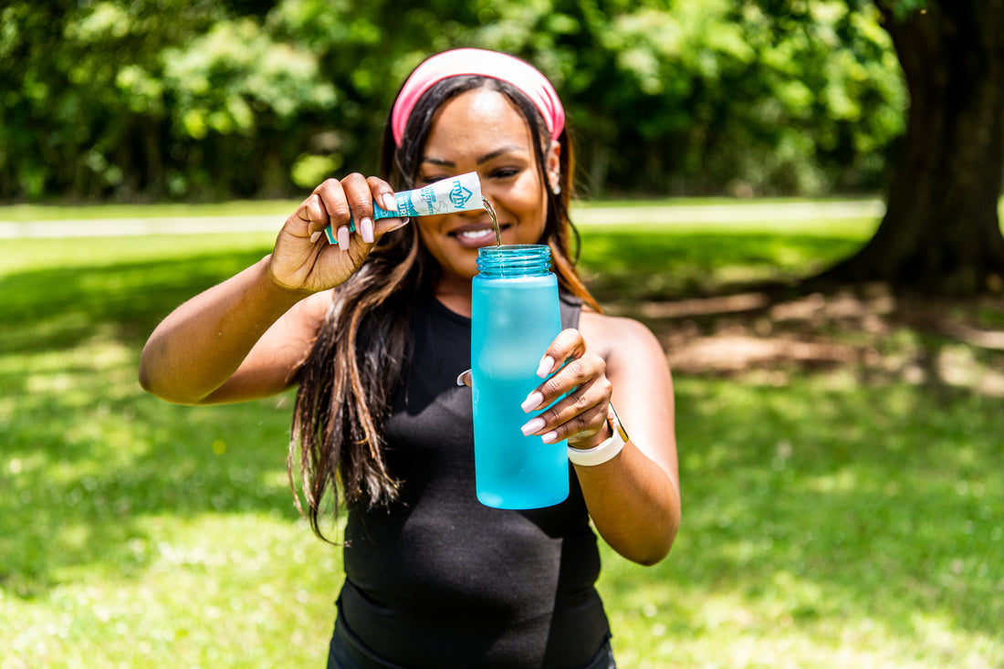 Woman pouring MyHy into water bottle in front of a tree in a park 